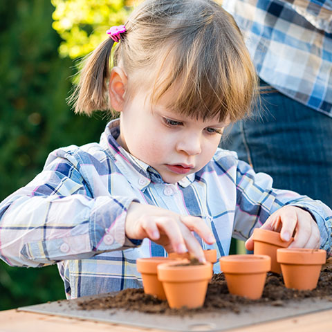 A young child carefully planting seeds in small pots